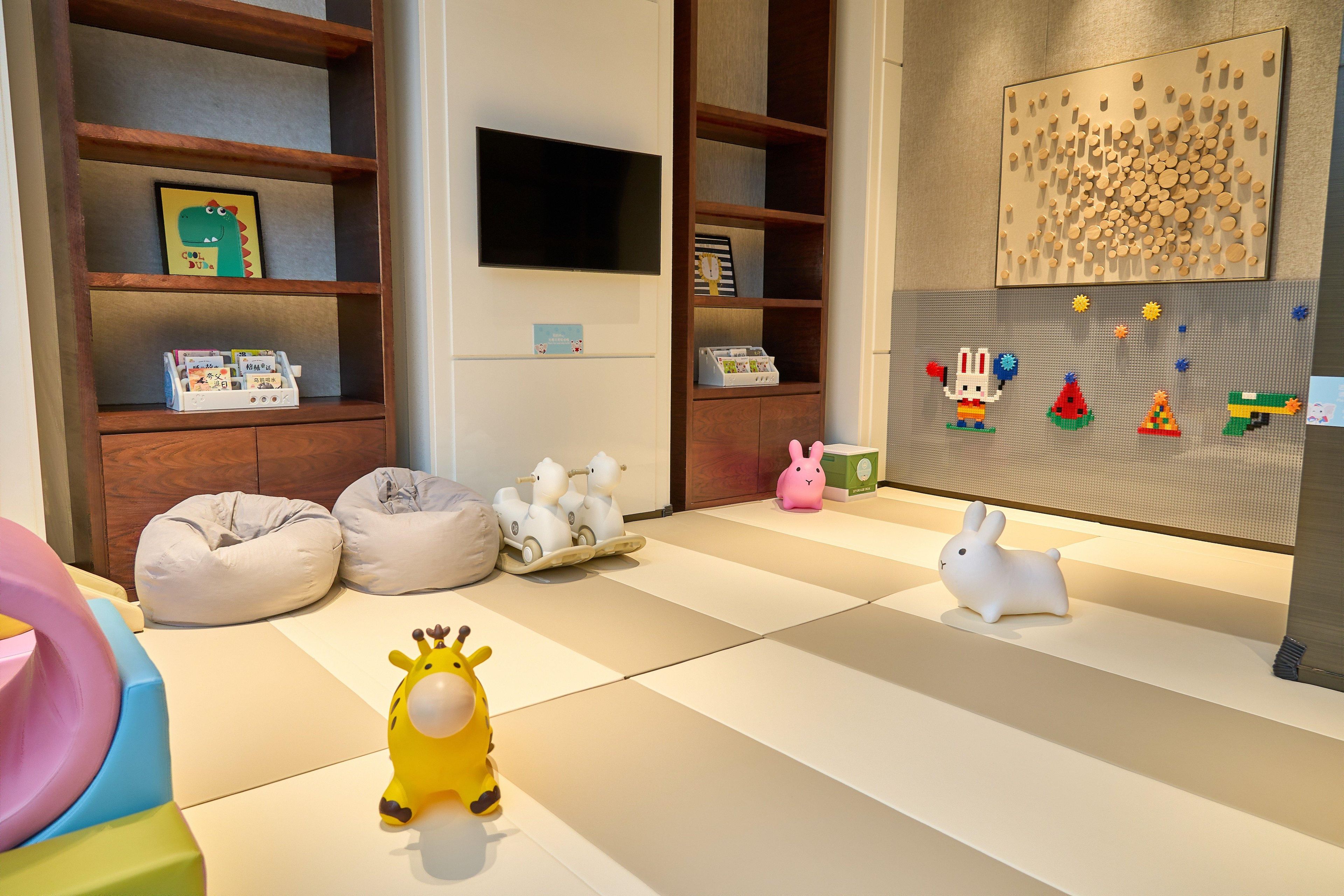 Un espace de jeux pour enfants avec des poufs, une voiture jouet et un jouet en forme de girafe.