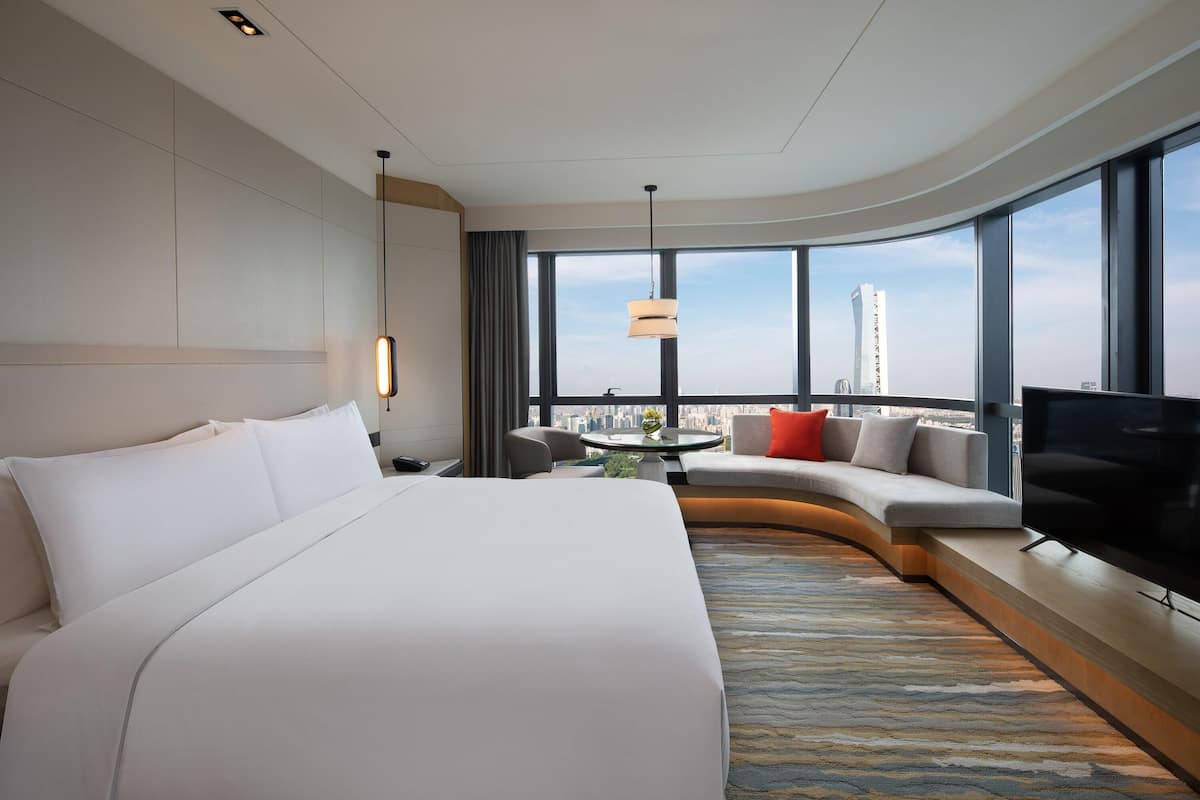 Quarto de hotel moderno com uma cama grande, um sofá, uma TV e vista para a cidade.
