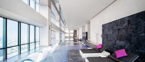 A modern indoor pool area with lounge chairs and a view of the city.