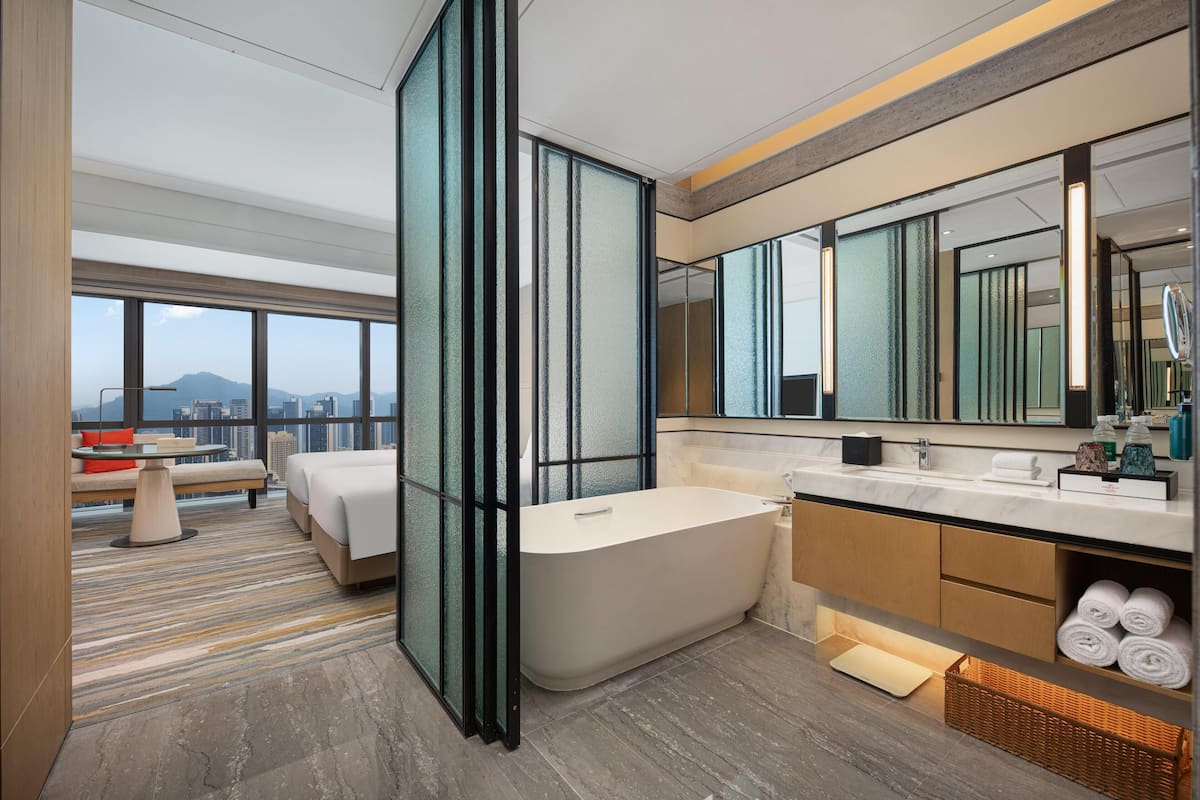 Um banheiro de hotel moderno com uma banheira separada, um espelho grande e vista para a paisagem urbana.