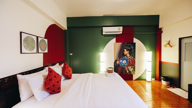 A hotel room with a bed, pillows, a wall-mounted air conditioner, and framed artwork. - Sleeper House (Trang)