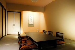 Um quarto japonês tradicional com tatames, uma mesa baixa e cadeiras pretas.