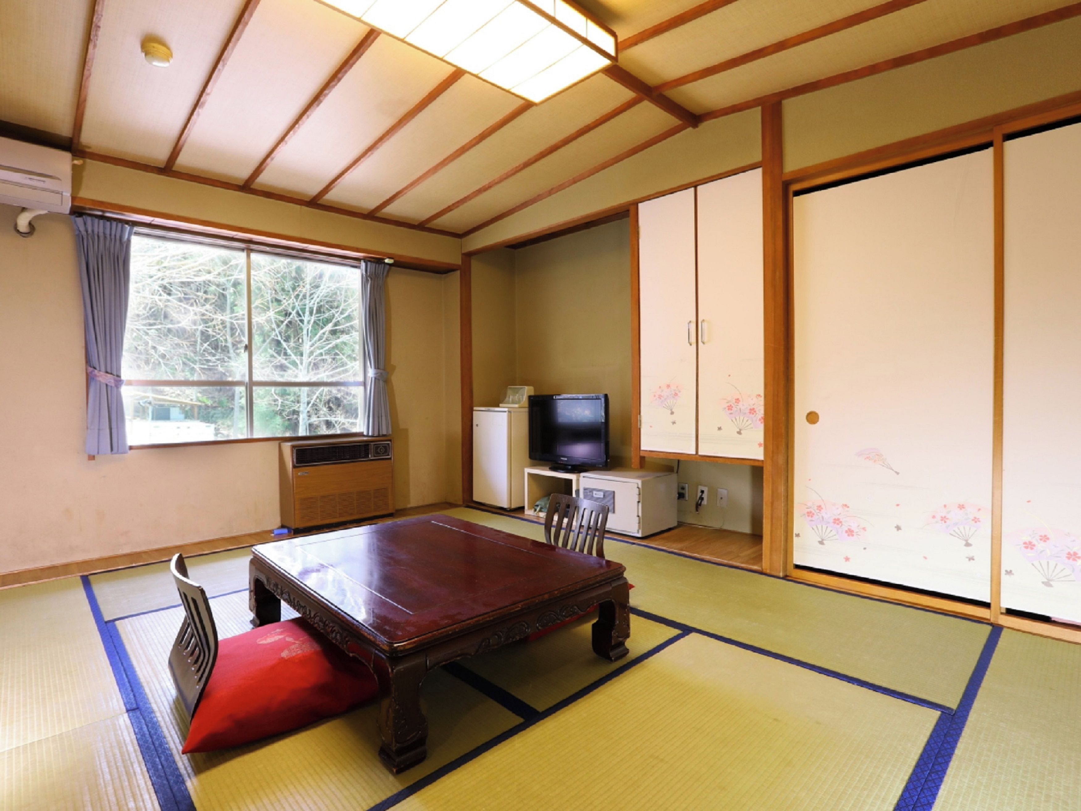 A traditional Japanese room with tatami flooring, a wooden table, a television, and sliding doors.