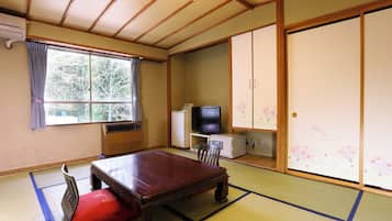 Una habitación japonesa tradicional con suelo de tatami, una mesa de madera, un televisor y puertas correderas.