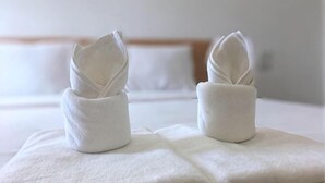 Two neatly folded towels on a bed with a wooden headboard and white pillows. - Bankhun Residence (Nakhon Ratchasima)