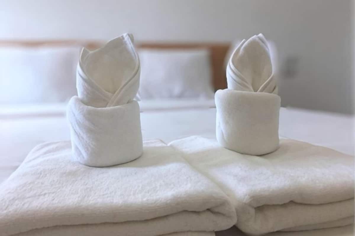 Two neatly folded towels on a bed with a wooden headboard and white pillows.
