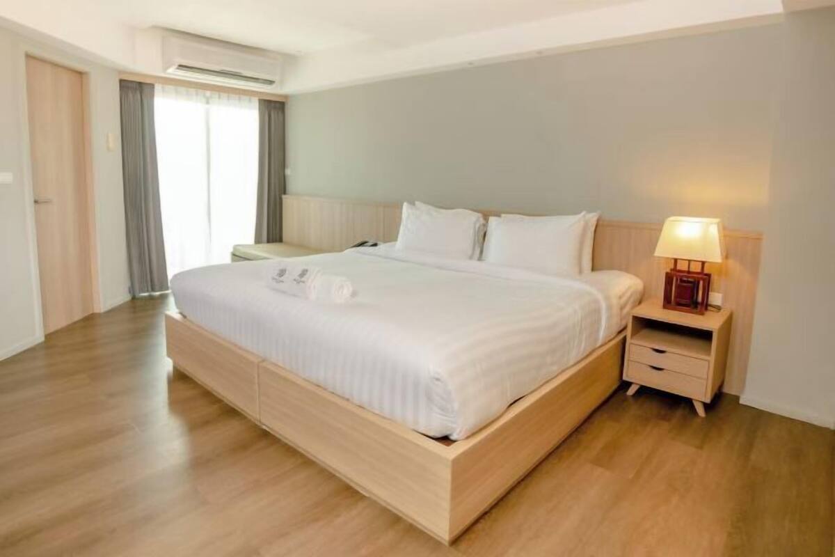 A hotel room with a wooden bed, a bedside table with a lamp, and a window with curtains.