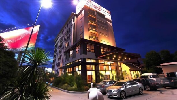 A multi-story hotel with a prominent sign, a parking area with several cars, and a large illuminated billboard in the background. - Bonito Chinos Hotel (Nakhon Sawan)