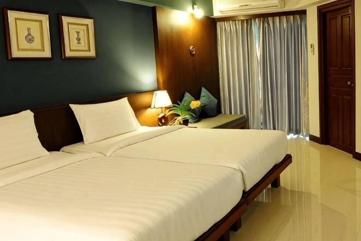 A hotel room with a large bed, a bedside table with a lamp, a wall-mounted air conditioner, and a door with a curtain.
