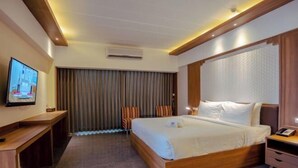 A hotel room with a large bed, a desk, a TV, and a window with curtains. - Bonito Chinos Hotel (Nakhon Sawan)