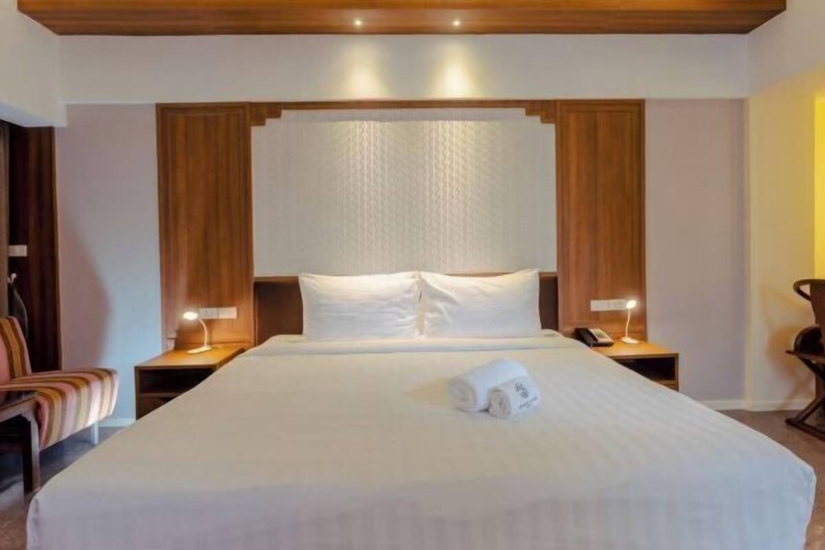 A hotel room with a large bed, two bedside tables with lamps, a chair, and a wooden headboard.