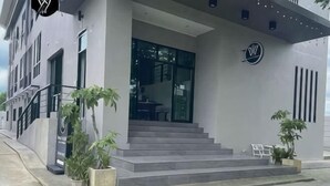 Um edifício moderno com uma escadaria que leva a uma entrada de vidro, plantas em vasos e um logotipo na parede.