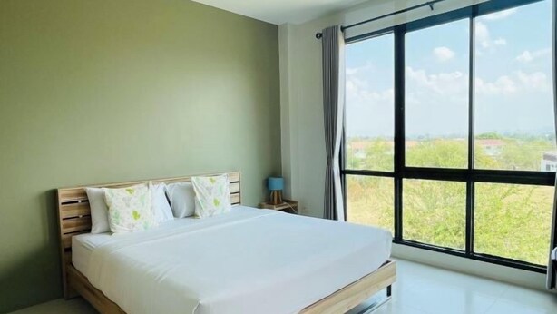 Quarto com cama grande, mesa de cabeceira, luminária e vista pela janela.