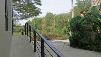 A balcony with a metal railing, a concrete floor, and a view of a road and greenery.