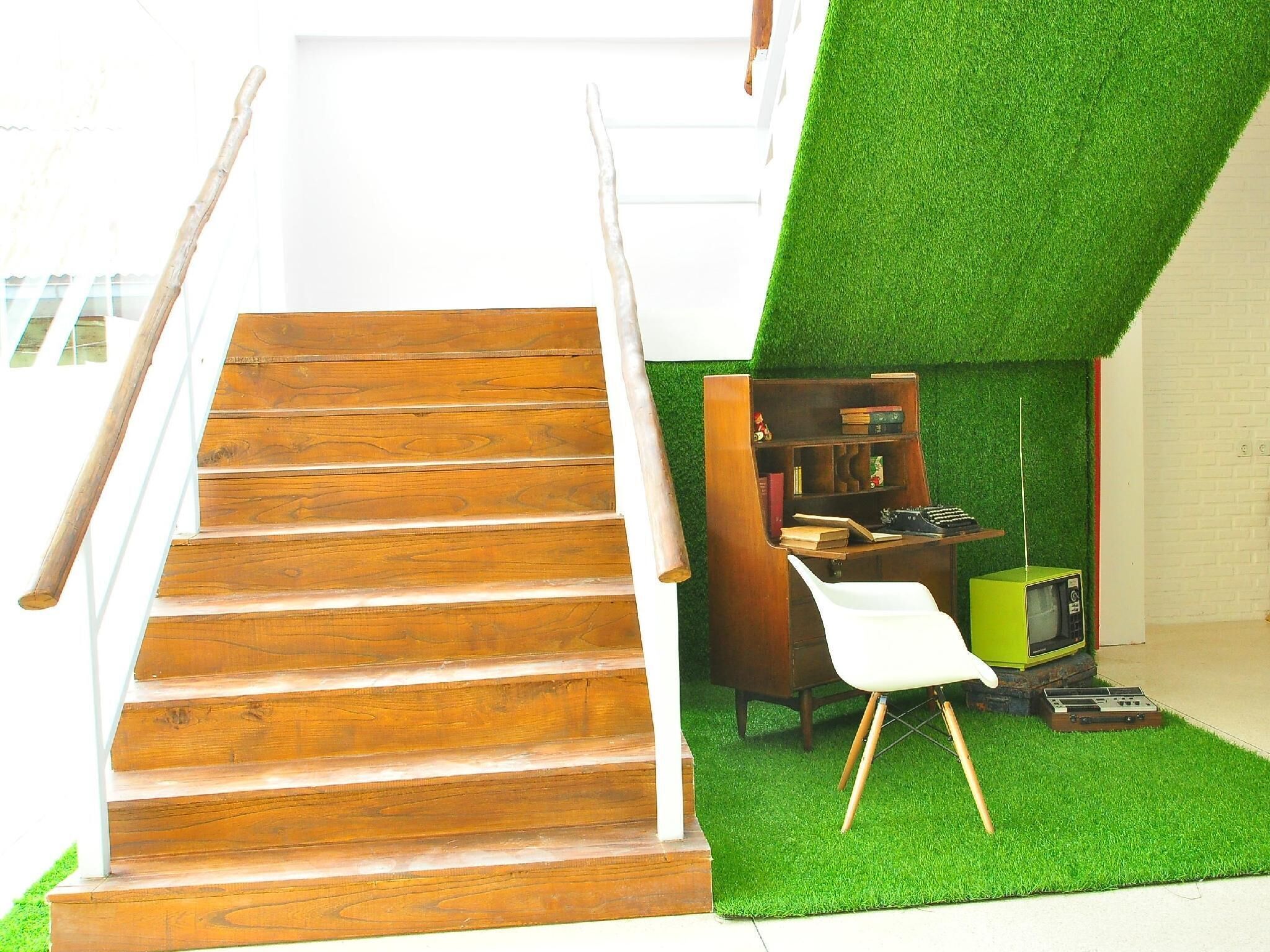 A staircase leading to a room with a green artificial grass floor, a wooden bookshelf, and a vintage green television.
