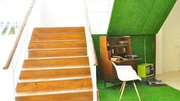 A staircase leading to a room with a green artificial grass floor, a wooden bookshelf, and a vintage green television.