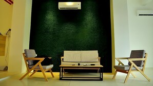 A modern room with a green textured wall, two wooden chairs, a striped sofa, and an air conditioning unit. - Summer Bed and Breakfast Hotel (Banjarmasin)