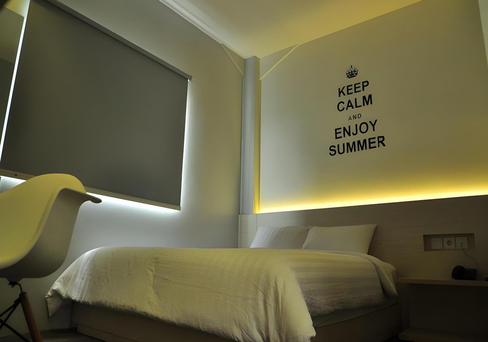A bedroom with a bed, a chair, a window, and a wall with a motivational quote.