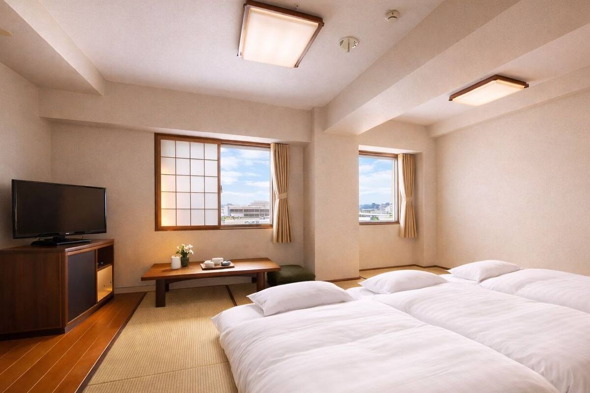 A hotel room with a TV, a desk, two beds, and large windows.