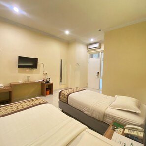 A hotel room with two beds, a desk, a television, and an air conditioning unit. - Riverstone Hotel & Cottage (Batu)