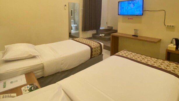A hotel room with two beds, a television, a mirror, and a small desk with a lamp. - Riverstone Hotel & Cottage (Batu)