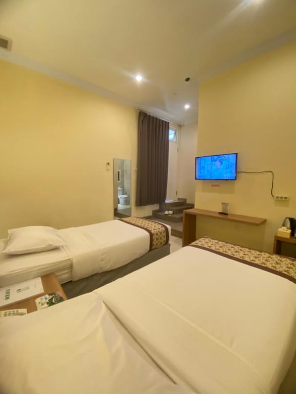 A hotel room with two beds, a television, a mirror, and a small desk with a lamp. - Riverstone Hotel & Cottage (Batu)