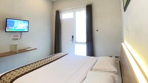 A hotel room with a bed, a television mounted on the wall, and a window with curtains. - Riverstone Hotel & Cottage (Batu)