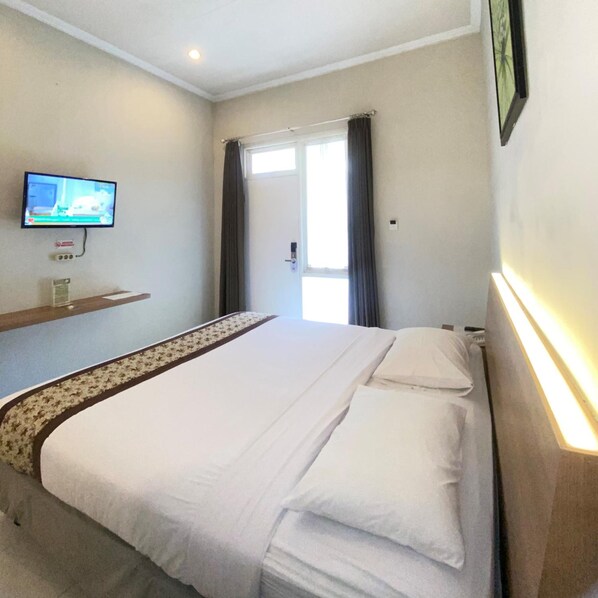 A hotel room with a bed, a television mounted on the wall, and a window with curtains.