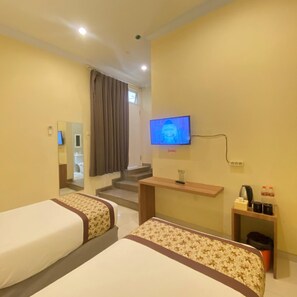 A hotel room with two beds, a TV, a desk with a computer, and a small trash bin.