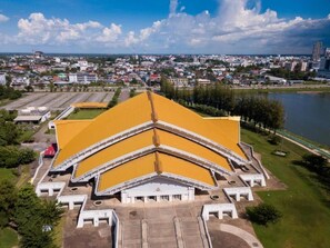 Un grand bâtiment à toit jaune, doté d’une cour intérieure, entouré d’un paysage urbain et bordé par une étendue d’eau.