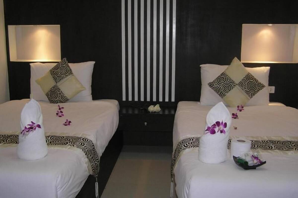 A hotel room with two beds, each with a pillow, a bedside lamp, and a towel with an orchid.