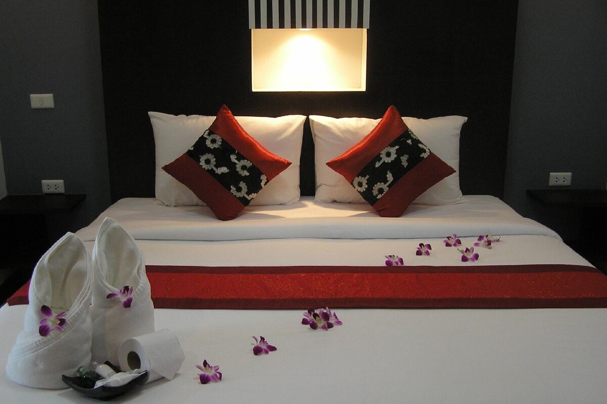 A hotel room with a bed, pillows, a nightstand, and a wall-mounted lamp.