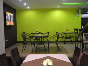 Un comedor con pared verde, televisor montado en la pared y ventilador de techo.