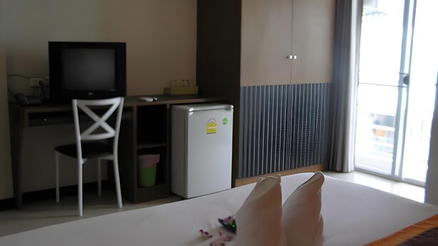 Hotellihuone, jossa on sänky, työpöytä tietokoneella, pieni jääkaappi ja tuoli.