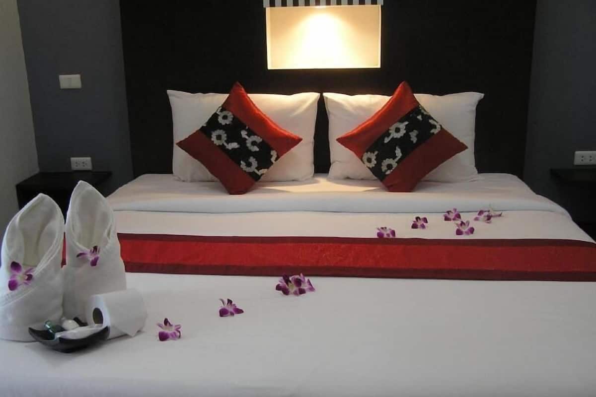 A neatly made bed with white linens and red accents, two decorative pillows, a bedside table, and a wall-mounted light fixture.