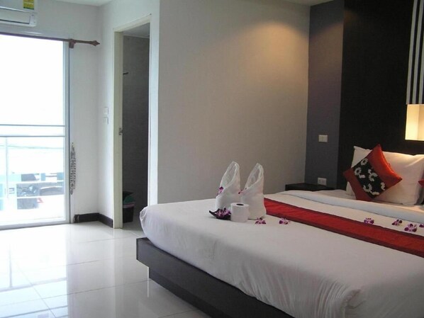 A hotel room with a bed, a nightstand, a lamp, a window, and a door.