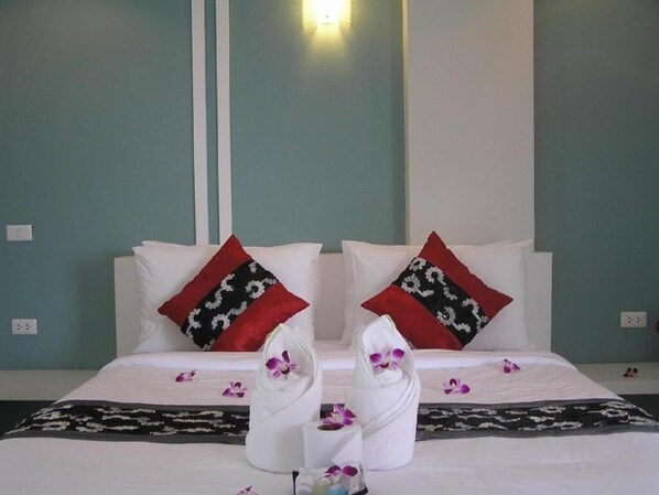 Une chambre d’hôtel avec deux lits, chacun agrémenté de draps blancs et d’oreillers aux motifs rouges et noirs. On trouve des serviettes et des fleurs sur les lits.
