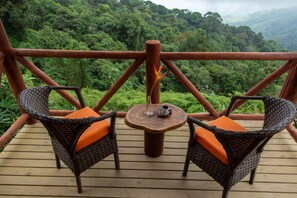 A wooden deck with wicker chairs and a table, overlooking a lush green forest. - Loma Nevada Minca Hotel (Santa Marta)