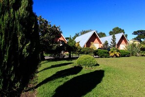 A row of red-roofed cabins with a well-maintained lawn and trees in the foreground. - Hotel Pousada Alto da Serra (Canela)