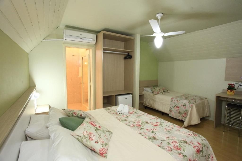 A room with two beds, a wardrobe, a desk, and a ceiling fan.