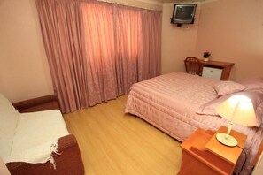 A bedroom with a bed, a desk, a chair, a television, and a window with curtains. - Hotel Pousada Alto da Serra (Canela)
