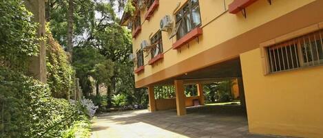 Um edifício com várias unidades de ar condicionado, um pátio pavimentado e vegetação ao redor.
