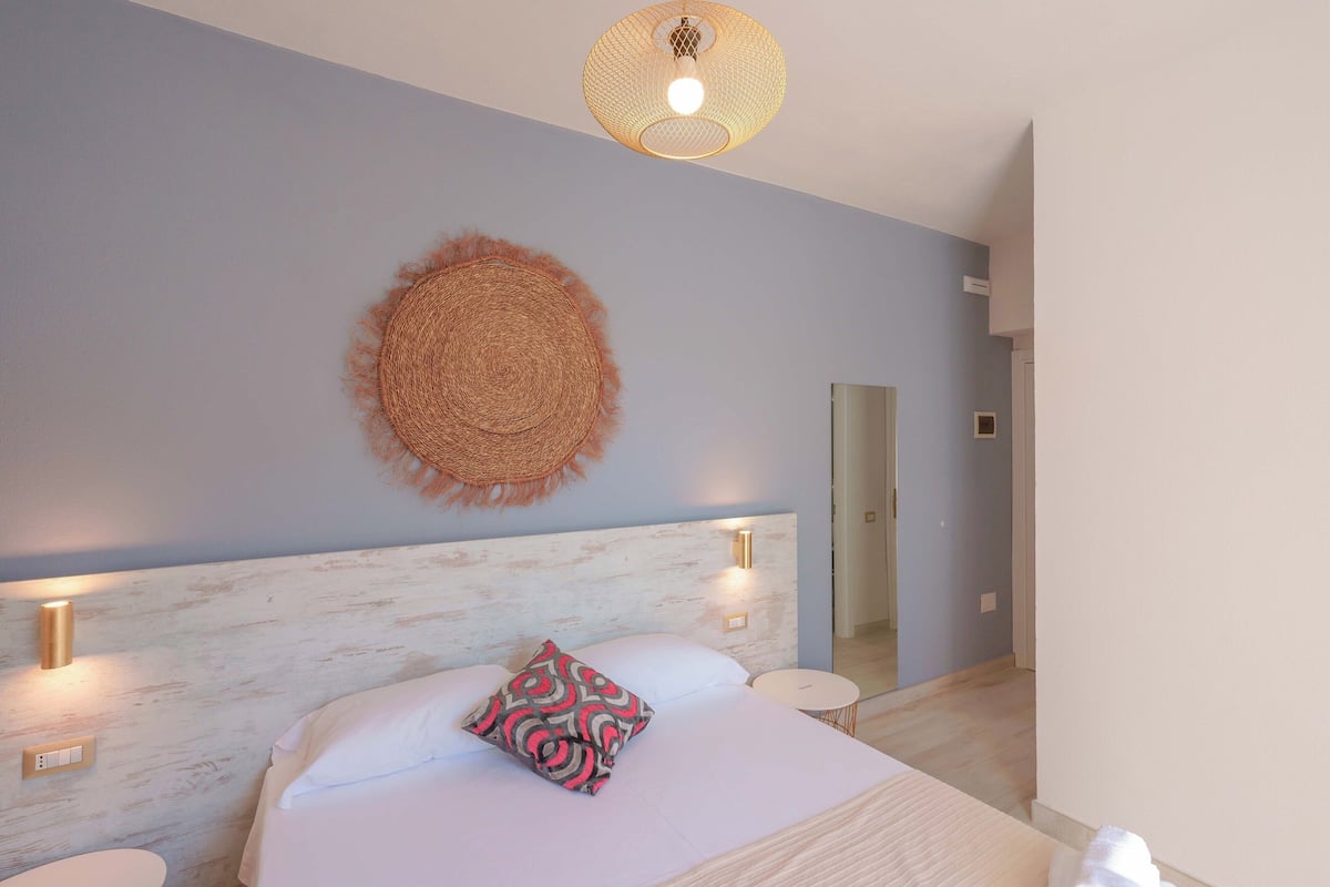 Un dormitorio con cama, mesitas de noche, una lámpara fijada a la pared y un adorno de pared tejido.