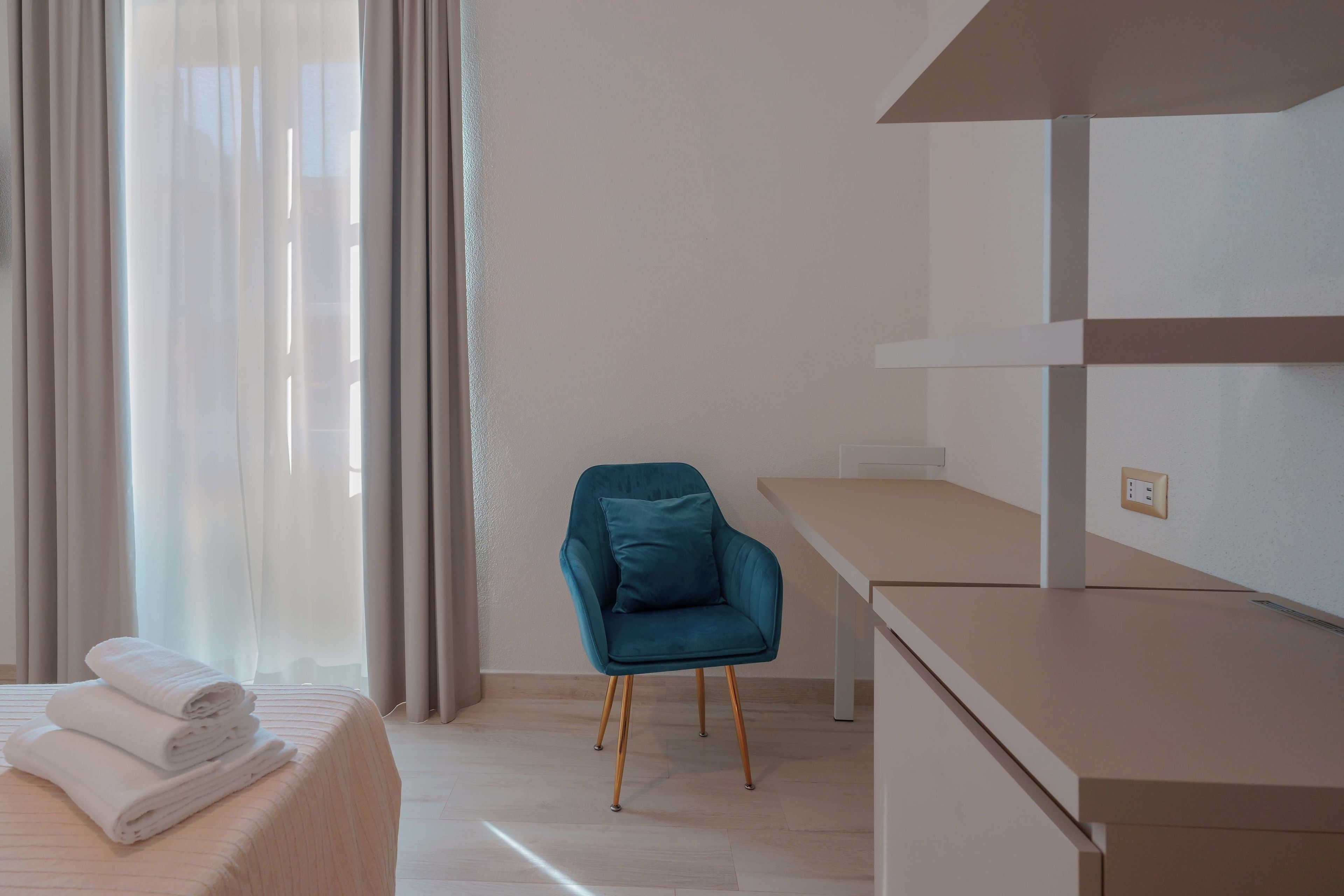 A hotel room with a bed, a desk, a chair, and a window with curtains.