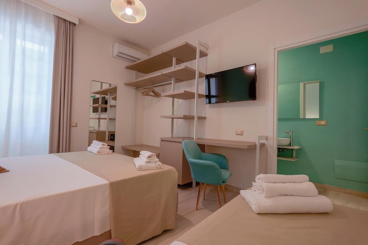 Habitación de hotel con dos camas, un escritorio, una silla, un televisor y un baño con pared verde.