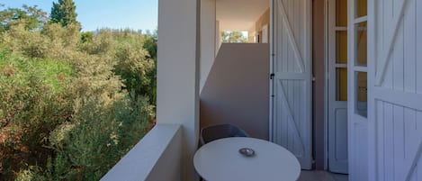 A balcony with a white table and chairs, a white door, and a view of trees and bushes.