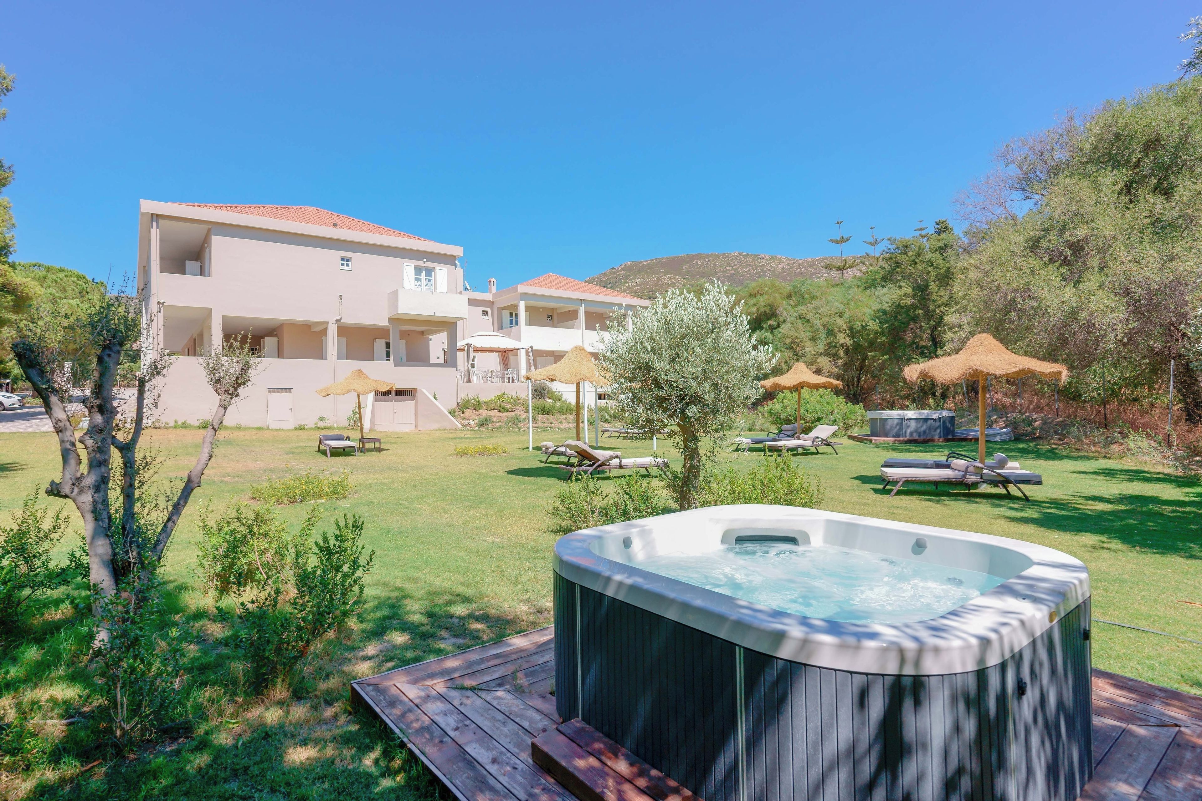 Un edificio moderno con un jacuzzi en el patio, rodeado de sillones de descanso y sombrillas.