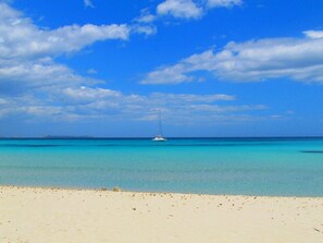 A beach with clear turquoise water and a sailboat in the distance. - Maison Del Sole (Quartu Sant'Elena)