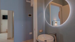 A bathroom with a round mirror, a sink, and a door leading to another room. - Maison Del Sole (Quartu Sant'Elena)