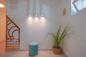 A hallway with a blue cylindrical object, a potted plant, and a geometric wall decoration. - Maison Del Sole (Quartu Sant'Elena)